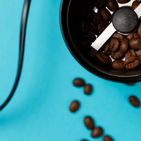 A tope view of an electric burr grinder with the lid off and coffee beans.