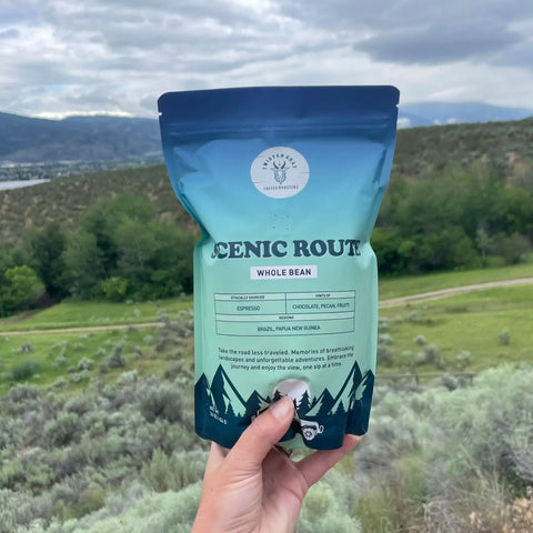 A person holding a bag of espresso beans called scenic route with a view of Oosyoos BC in the background.