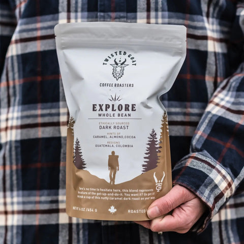 A women holding a bag of dark roast coffee beans in a flannel shirt