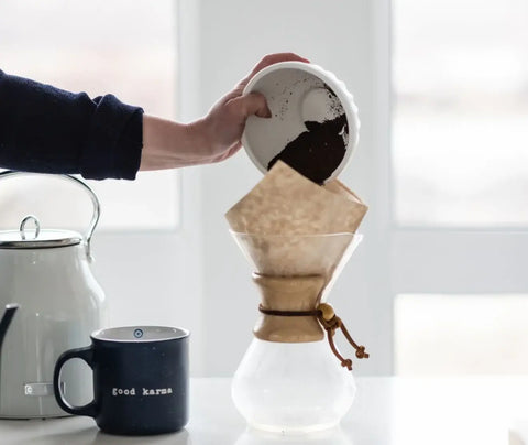 A person adding coffee grounds to a chemex coffee maker