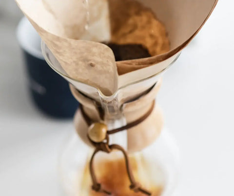 A person adding water to a coffee maker to first wet the grounds