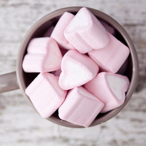 A coffee mug filles with pink valentines day heart marshmallows.