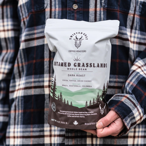 a women holding a bag of decaf coffee wearing a flannel shirt.