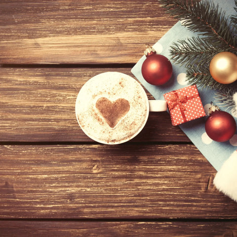 A latte with a heart decoration for Christmas beside a tree.
