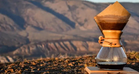 A Chemex coffee maker sitting outdoors with a background view of Kamloops BC hoodoos.