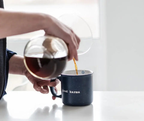 A person pouring coffee into a coffee mug from a chemex coffee maker