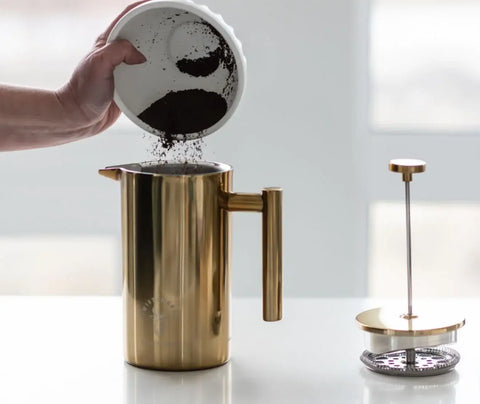 a person adding coarse ground coffee to a french press to show how to use a french press