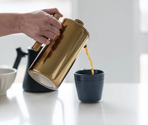 a person pouring coffee into a coffee mug from a french press 