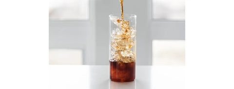 Someone pouring cold brew coffee into a glass full of ice.