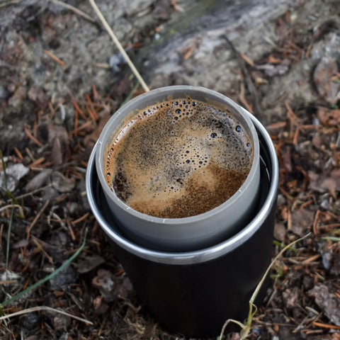 A view of a hot cup of coffee sitting on the ground in nature.